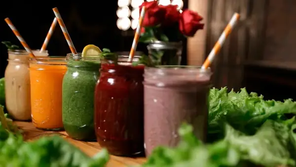 Fem färgglada smoothies i glasburkar, redo för en bebis att njuta av. Grönt, orange, rött och lila.