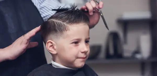 Chłopiec w salonie fryzjerskim, gdzie powstają modne fryzury dla chłopców 8 lat. Fryzjerka modeluje jego włosy.