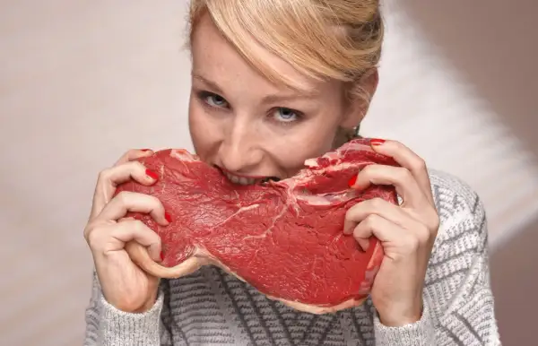 Kobieta z rudymi włosami i piegami wgryza się w surowy kawałek mięsa, jakby to była jej dieta lwa.