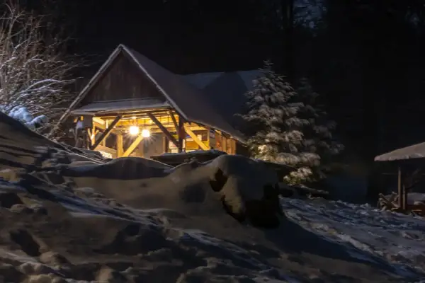 Zimowa noc. Oświetlona chata pod potrójną, otoczona śniegiem i drzewami.