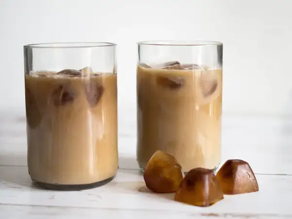 Två glas med iskaffe, perfekt för ett enkelt iskaffe recept. Tre kaffekuber ligger framför.