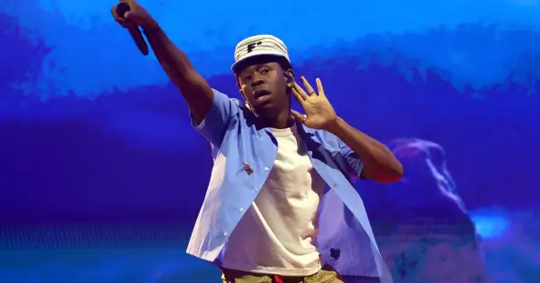 Tyler The Creator w Krakowie, w niebieskiej koszuli i czapce, z mikrofonem w dłoni.