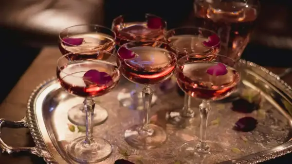 Eleganckie kieliszki z różowym winem, ozdobione płatkami róży, czekają na degustację. W tle widać karafkę z tym samym trunkiem, być może to wykwintny tokaji aszu.