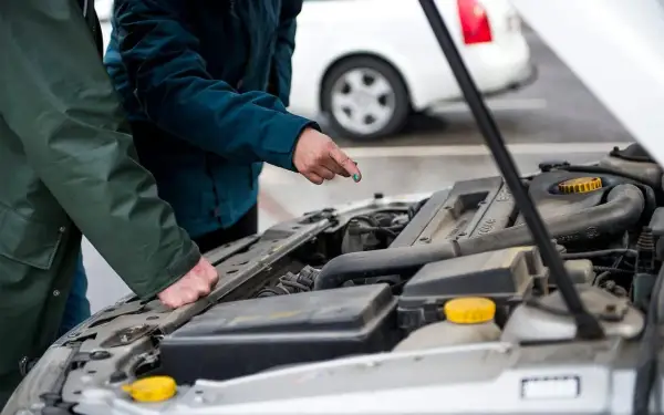 Två personer gör en bil kontroll vid en öppen motorhuv. En pekar på något i motorn.