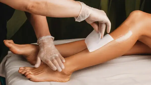 Una mano guantata applica una striscia di cera su una gamba. Per una ceretta efficace, i peli devono essere lunghi circa mezzo centimetro.