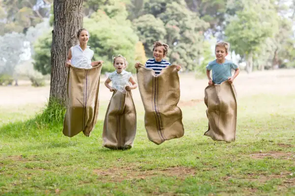 Niños compiten en una divertida carrera de sacos en un día soleado en el parque.