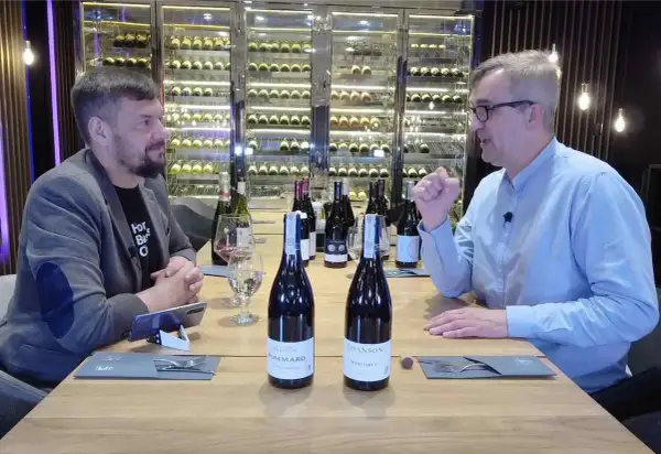Dwóch mężczyzn przy stole degustuje wino. Na stole stoją butelki, w tym dwie z etykietami sugerującymi pinot noir.