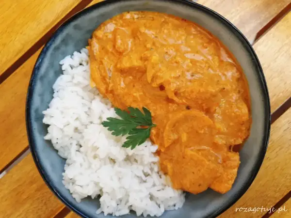 Aksamitny butter chicken w kremowym sosie, podany z ryżem i listkiem pietruszki. Pyszne danie na drewnianym stole.