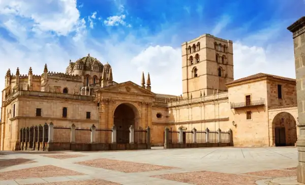 Imponente catedral románica en España, con su torre campanario y cúpula, bajo un cielo azul con nubes.
