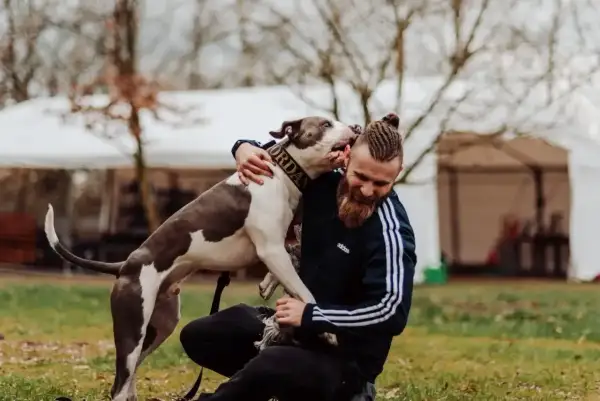 Mężczyzna z brodą i warkoczami przytula psa. Pies ma obrożę z napisem "Jordan". Szukając imiona dla psa, warto inspirować się tym, co kochamy.