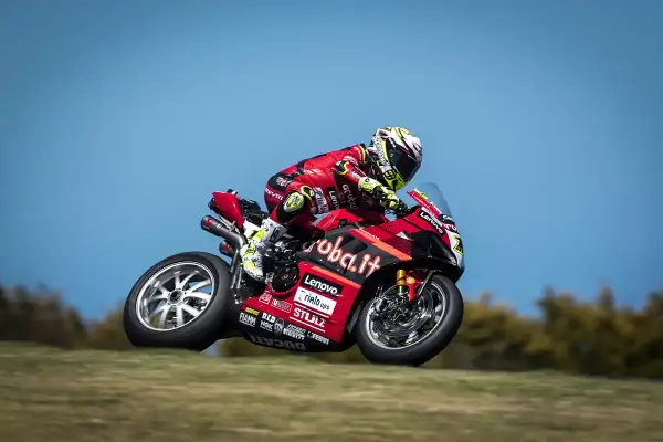Piloto de SBK hoy en acción, con su moto Ducati roja y negra, inclinándose en una curva.
