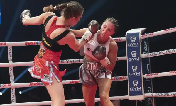 Two female boxers in a strawweight boxing match exchange punches in the ring. One boxer lands a blow to the other's face.