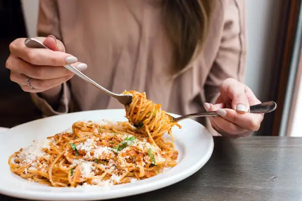 Une personne déguste une assiette de spaghetti à la sauce tomate et au parmesan. Une recette de pâtes parfaite pour un repas réconfortant.