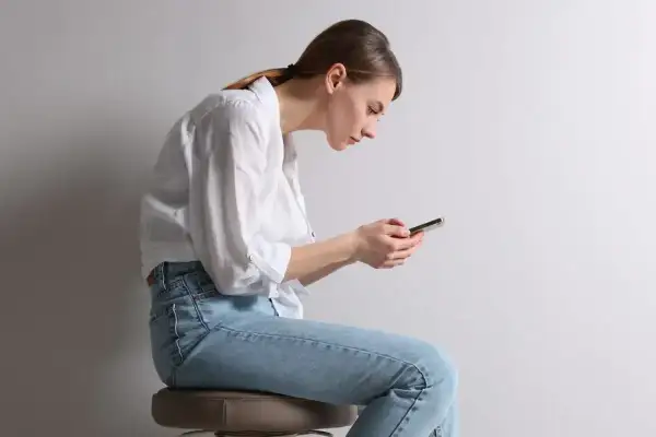 Frau mit gebeugtem Rücken und Handy, die Haltung erinnert an einen Stiernacken.