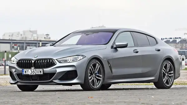 Szary BMW M8 Gran Coupe z czarnym dachem i felgami, zaparkowany na ulicy.