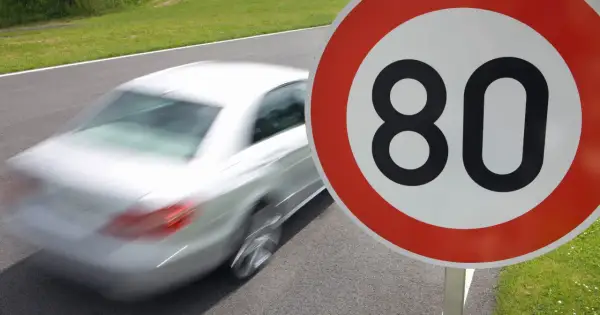 Znak ograniczenia prędkości do 80 km/h. Biały samochód pędzi po drodze, przypominając o przepisach ruchu drogowego i ograniczeniach prędkości w Polsce.