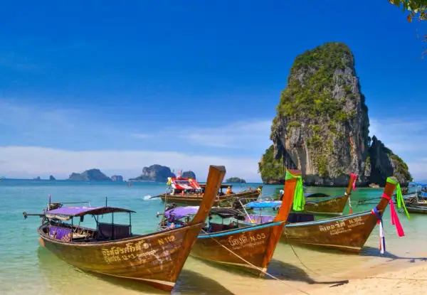 Träbåtar guppar i det turkosa vattnet vid Koh Hong. En imponerande klippa reser sig ur havet.