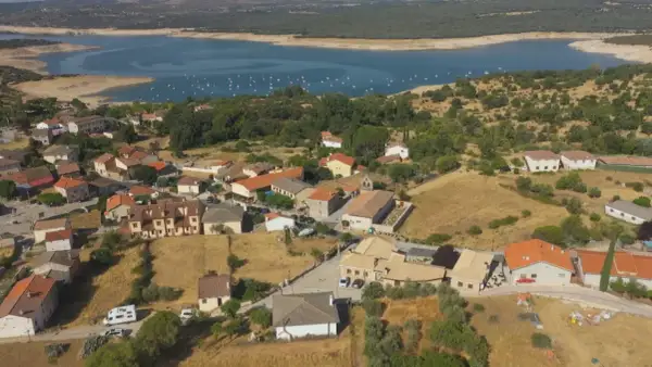 Vista aérea de Cervera de Buitrago, con casas de tejados naranjas y un embalse azul al fondo.