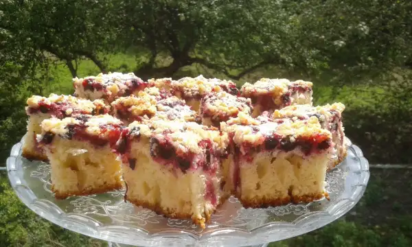 Pyszne ciasto z czarnymi porzeczkami i kruszonką, posypane cukrem pudrem, na szklanej paterze.