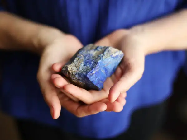 Manos sostienen un trozo de lapislázuli, su intenso azul resalta contra la tela azul.