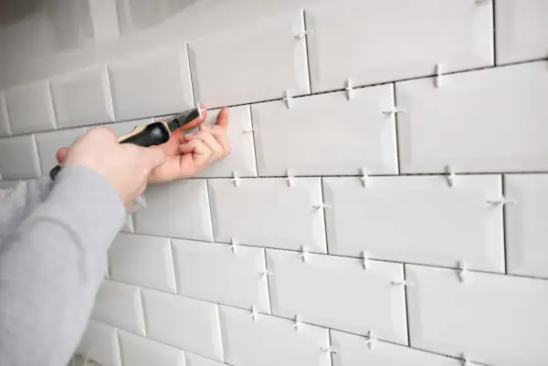 Pose de carrelage blanc avec des croisillons pour assurer un espacement parfait. Un outil est utilisé pour ajuster le **taille croisillon carrelage**.