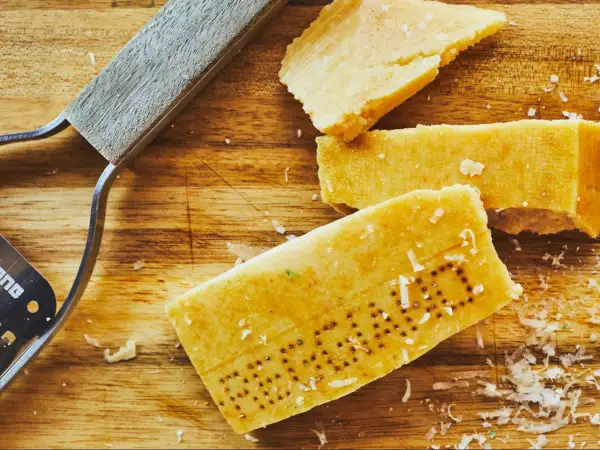 Des morceaux de **croûte parmesan comestible** sur une planche en bois, avec un râpe à fromage.