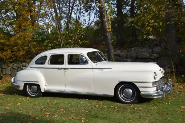 En vit Chrysler New Yorker från 1940-talet står parkerad på en gräsmatta med höstlöv.