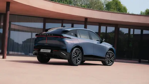 Lancia Gamma 2026, un'elegante berlina blu metallizzato con fari posteriori a LED, parcheggiata davanti a un edificio moderno.