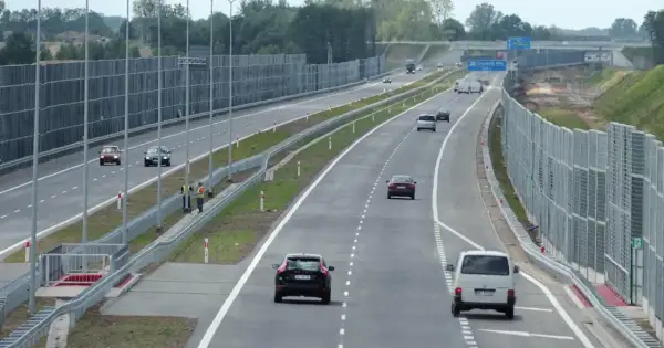 Samochody poruszają się lewym pasem w terenie zabudowanym, mijając ekrany akustyczne.