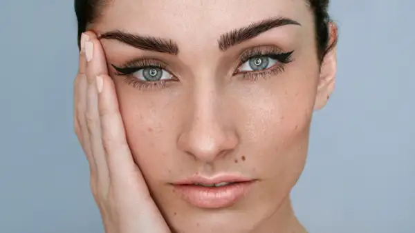 Rostro de mujer con microblading cejas perfectas, delineado de ojos y piel con pecas.
