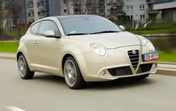 Złoty Alfa Romeo MiTo w ruchu miejskim. Wiele osób chwali ten model za wygląd, co potwierdzają alfa romeo mito opinie.