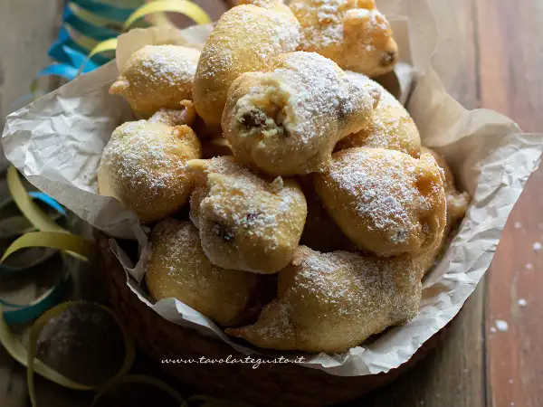 Frittelle di una volta, dolci e soffici, cosparse di zucchero a velo, in un cesto con coriandoli.