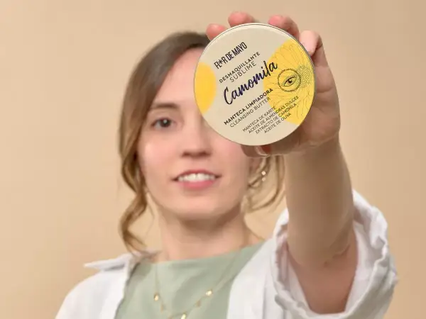 Mujer sonriente sostiene un desmaquillante en crema, "Camomila", que es un sebo limpiador con manteca de karité.