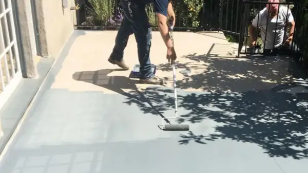 Peinture carrelage extérieur avant après : un homme peint une terrasse grise avec un rouleau, transformant l'espace.