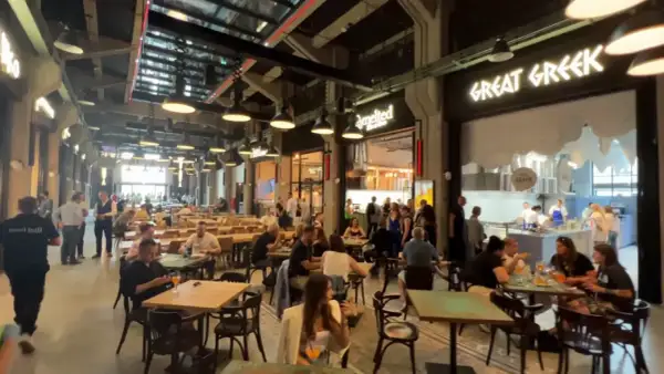 Tętniący życiem food hall w Gdańsku. Ludzie siedzą przy stołach, jedzą i rozmawiają. W tle widać lokal "Great Greek".