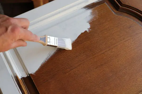 Mano che dipinge con pennello bianco su mobile in legno scuro. La cementite a cosa serve? A preparare la superficie per una finitura perfetta.