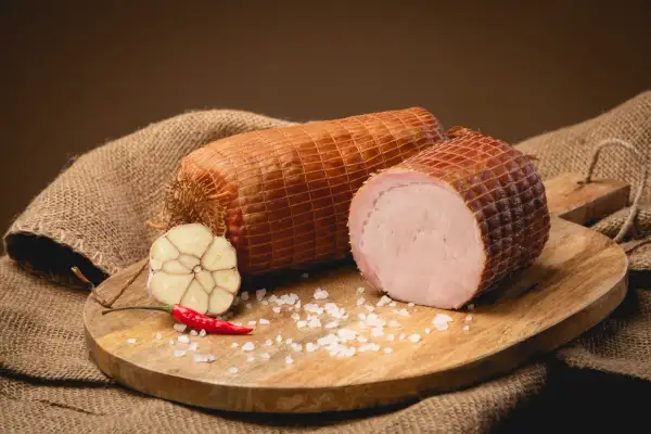 Dwie wędzone szynki na desce, obok czosnek, papryczka chili i sól. Idealne składniki, by dowiedzieć się, jak wędzić szynkę.