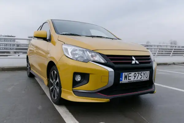 Żółty Mitsubishi Space Star 2004 z czarnym grillem i czerwonymi akcentami stoi na parkingu.