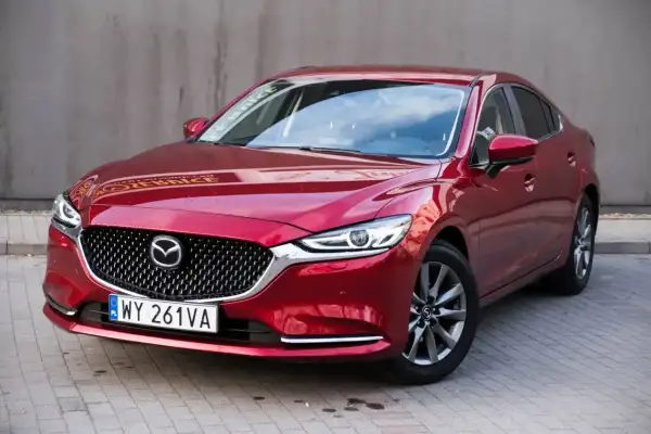 Czerwona Mazda 6 2.0 benzyna z eleganckim grillem i nowoczesnymi światłami, zaparkowana na kostce brukowej.
