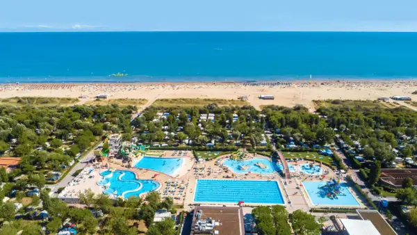 Widok z lotu ptaka na plażę i kompleks basenów w **marina do Venezia**. Widać morze, piaszczystą plażę z leżakami, camping i zjeżdżalnie wodne.