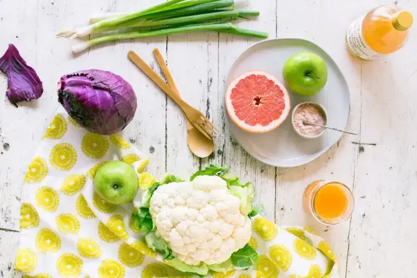 Jabłka i grejpfruty to owoce, które pomagają obniżyć cholesterol. Na zdjęciu widzimy też kalafior, czerwoną kapustę i szczypiorek.