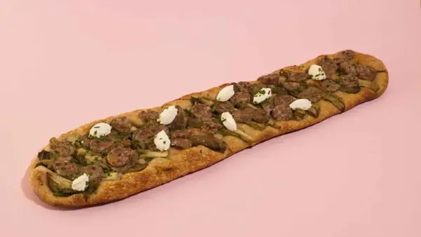 Deliciosa coca de recapte con salchicha, alcachofas y queso de cabra, lista para compartir.