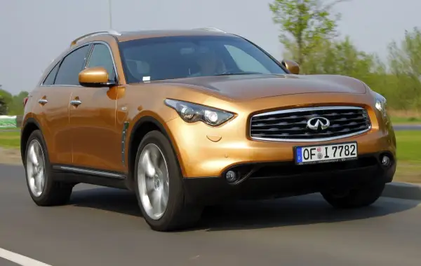 Złoty Infiniti FX35 pędzi po drodze, jego sylwetka jest dynamiczna i sportowa.