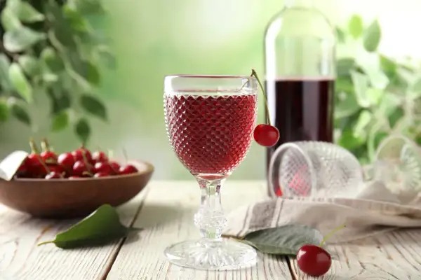 W kieliszku wiśniowy napój, a obok miska pełna owoców. To właśnie z nich robi się wino, które w butelce czeka na degustację.