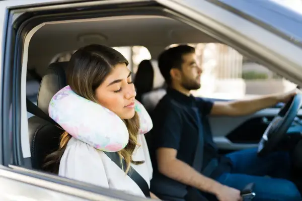 Donna dorme in auto con un cuscino cervicale fai da te, mentre l'uomo guida.