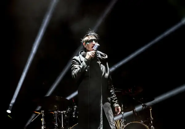 Marilyn Manson na scenie w Warszawie, w czarnym płaszczu i z charakterystycznym makijażem, śpiewa do mikrofonu.