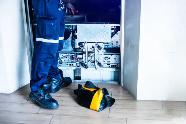 Tecnico ripara un ascensore guasto, impedendo l'accesso ai disabili. La borsa degli attrezzi è a terra.