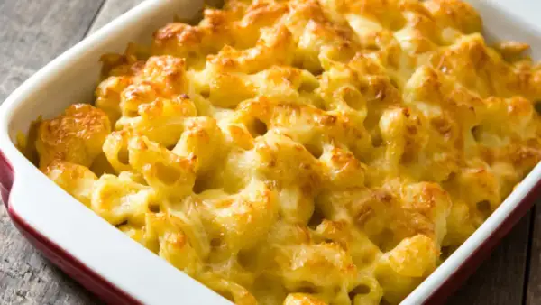Mac and cheese cremoso y dorado, recién salido del horno en una fuente roja.