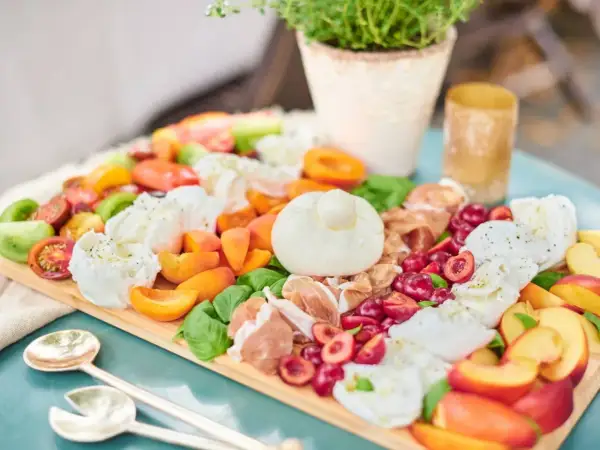 Antipasti-Platte mit Kerze, Wurst, Käse, Oliven und Brot auf Holztisch.