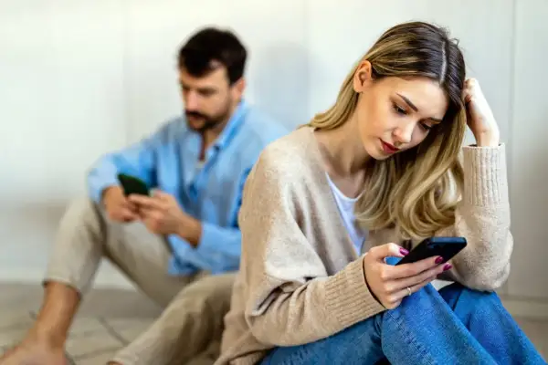 Een vrouw en man zitten apart, beiden op hun telefoon. Ze voelen zich leeg in hun relatie, de afstand tussen hen is voelbaar.